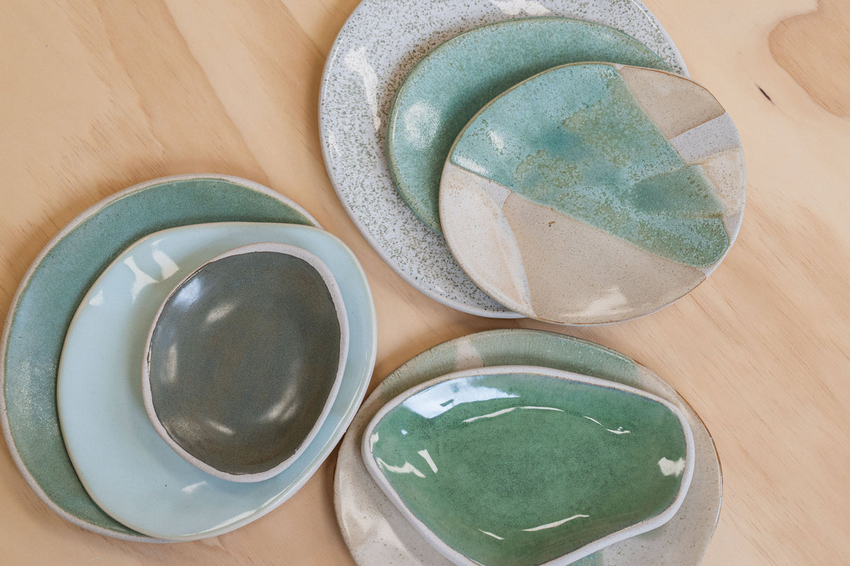 Stacked handmade stoneware platters in sea green, pale celadon-blue and slate grey on a timber table